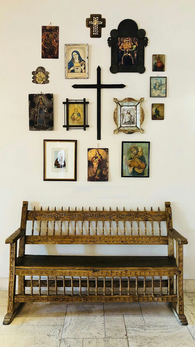 Religious paintings and crosses hang above an antique wooden bench.