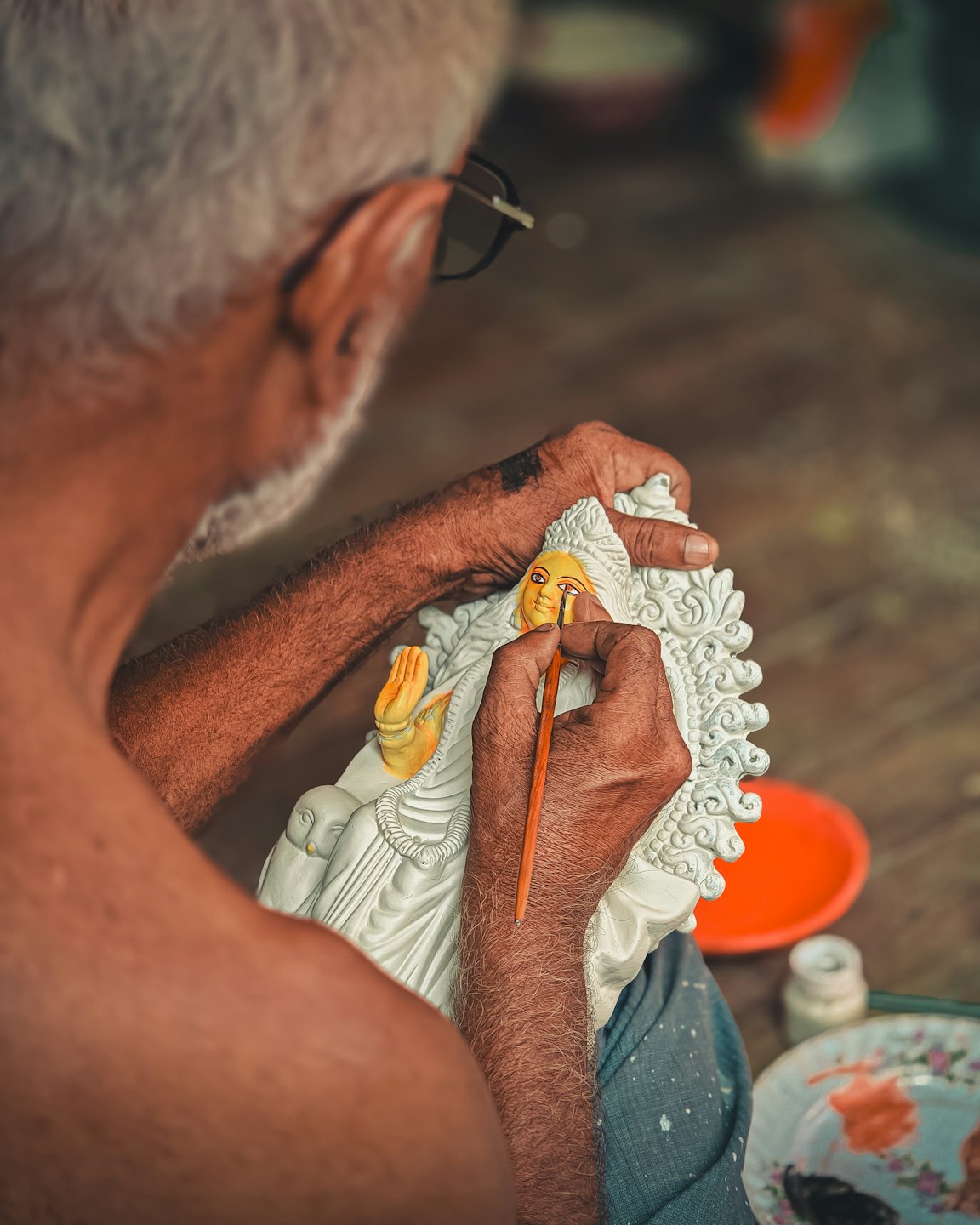 Artisan painting details on a sculpted deity idol's face.